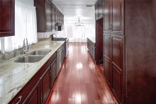 kitchen featuring visible vents, light stone countertops, dark wood finished floors, stainless steel gas range, and a sink