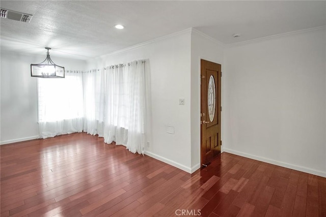 spare room with visible vents, crown molding, baseboards, wood finished floors, and a notable chandelier