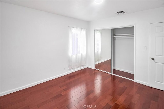 unfurnished bedroom with a closet, visible vents, baseboards, and wood finished floors