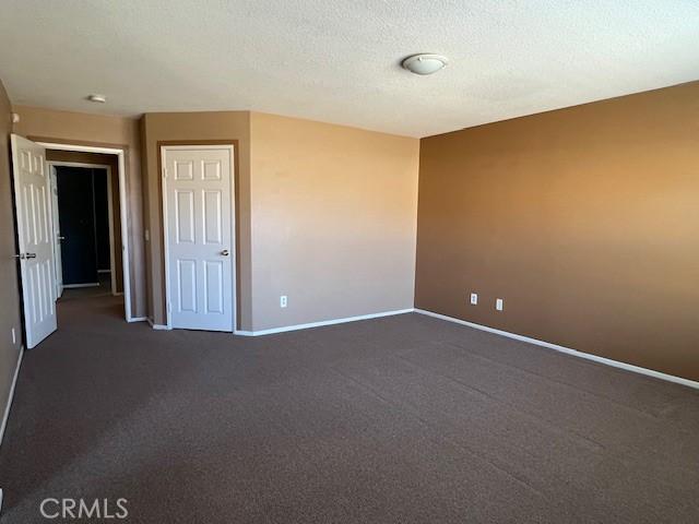 empty room with dark carpet, a textured ceiling, and baseboards