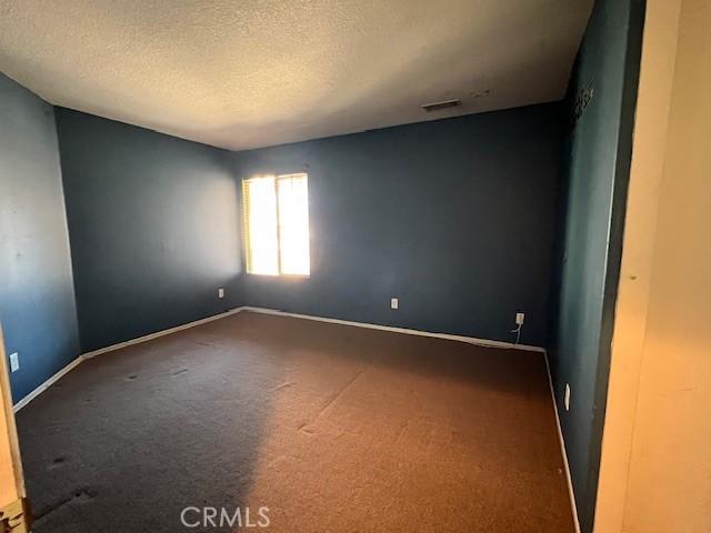 empty room featuring visible vents, a textured ceiling, baseboards, and carpet floors