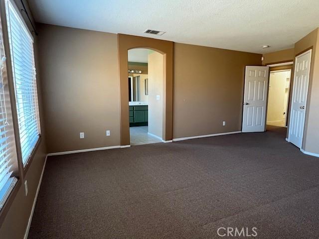 unfurnished room with visible vents, baseboards, arched walkways, a textured ceiling, and dark colored carpet