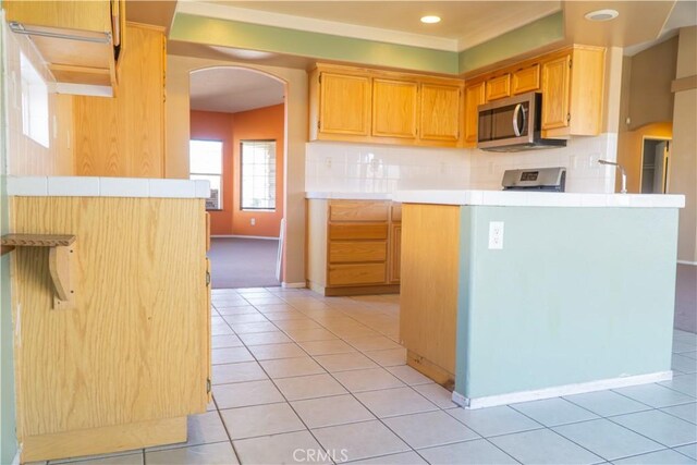 kitchen with stainless steel microwave, arched walkways, light tile patterned flooring, decorative backsplash, and recessed lighting