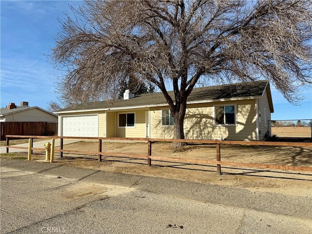 single story home featuring a chimney, concrete driveway, an attached garage, and fence