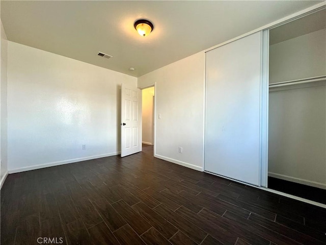 unfurnished bedroom with a closet, visible vents, dark wood-type flooring, and baseboards