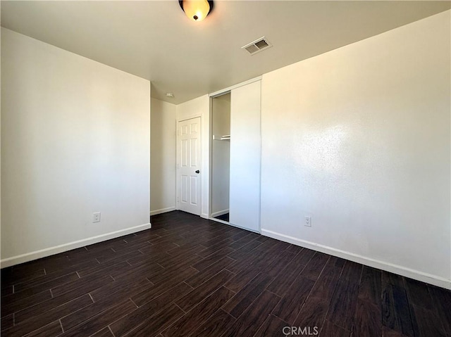 unfurnished bedroom featuring visible vents, baseboards, a closet, and dark wood-style flooring