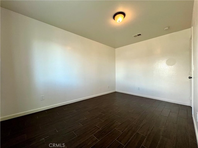 unfurnished room featuring dark wood-style floors, visible vents, and baseboards