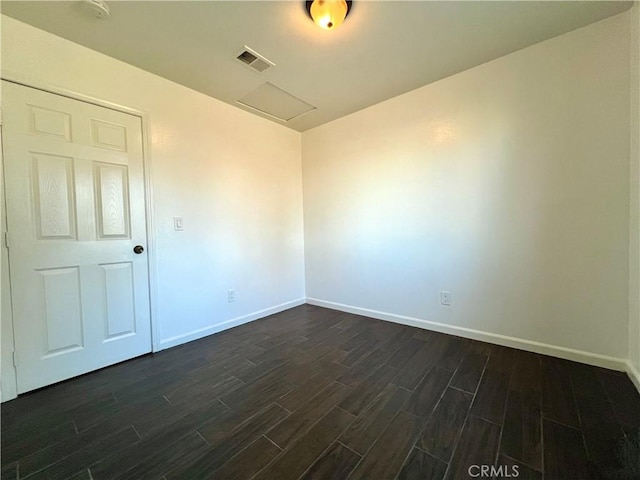 spare room with visible vents, baseboards, attic access, and dark wood finished floors