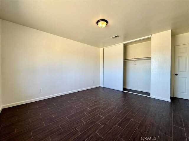 unfurnished bedroom with dark wood finished floors, baseboards, visible vents, and a closet