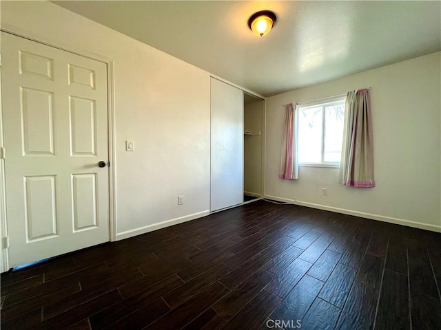 unfurnished bedroom featuring dark wood-type flooring, baseboards, and a closet