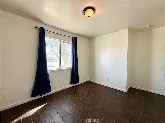 empty room featuring baseboards and dark wood finished floors