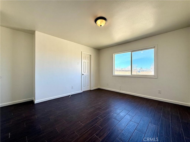 empty room featuring dark wood-type flooring and baseboards