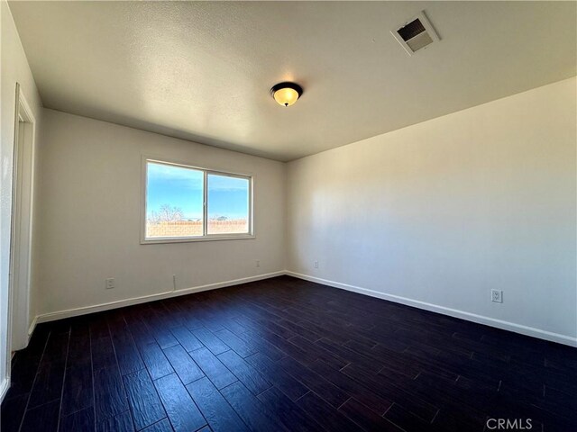 empty room featuring visible vents, baseboards, and dark wood-type flooring