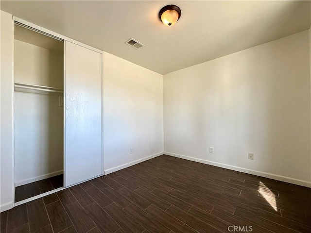 unfurnished bedroom with dark wood-style floors, visible vents, baseboards, and a closet