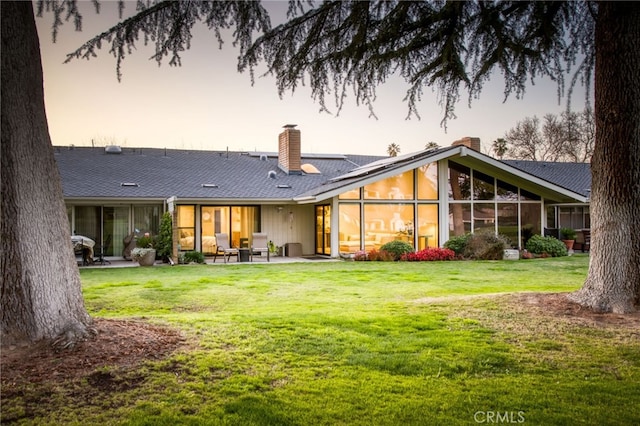 rear view of house featuring a patio, a yard, and a chimney