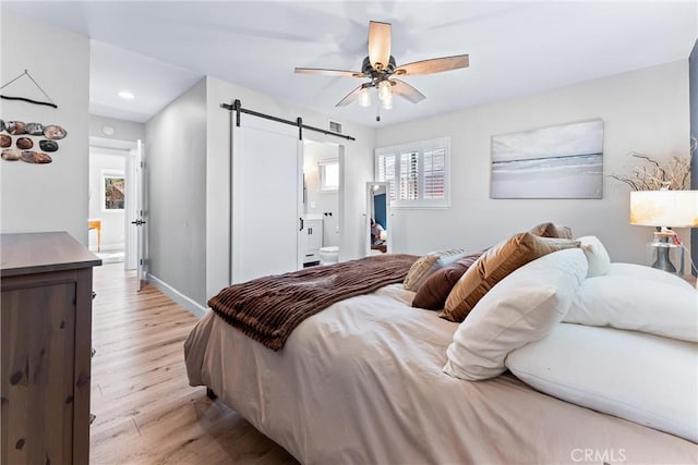 bedroom featuring baseboards, light wood-style flooring, recessed lighting, a barn door, and connected bathroom