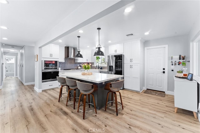 kitchen with a kitchen island, light countertops, white cabinets, stainless steel appliances, and wall chimney exhaust hood