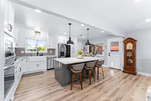 kitchen featuring light wood finished floors, a kitchen island, a sink, decorative backsplash, and appliances with stainless steel finishes