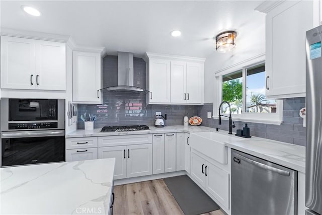 kitchen with white cabinets, stainless steel appliances, wall chimney range hood, and a sink