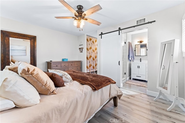 bedroom featuring visible vents, ceiling fan, light wood-style floors, ensuite bathroom, and a barn door