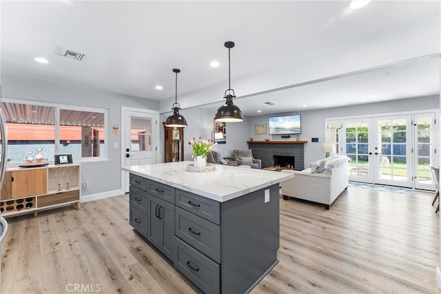 kitchen with light wood-style flooring, gray cabinets, a center island, french doors, and a brick fireplace