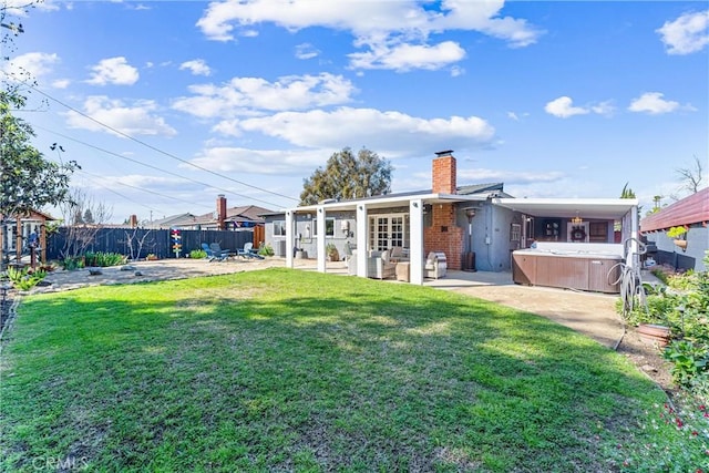 back of house featuring a patio, a yard, a fenced backyard, a chimney, and a hot tub