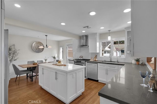 kitchen with a wealth of natural light, wall chimney exhaust hood, appliances with stainless steel finishes, and a sink