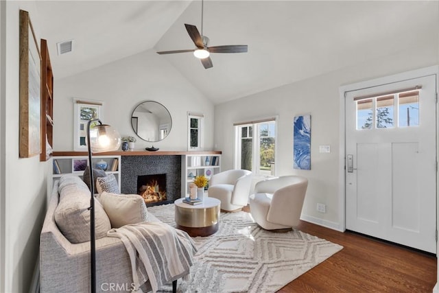 living area featuring visible vents, baseboards, dark wood finished floors, a warm lit fireplace, and a ceiling fan