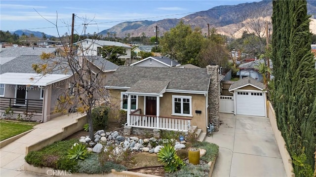 single story home featuring a mountain view, covered porch, concrete driveway, a shingled roof, and a garage