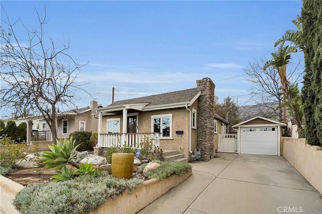 view of front of property featuring stucco siding, driveway, a detached garage, a porch, and an outdoor structure