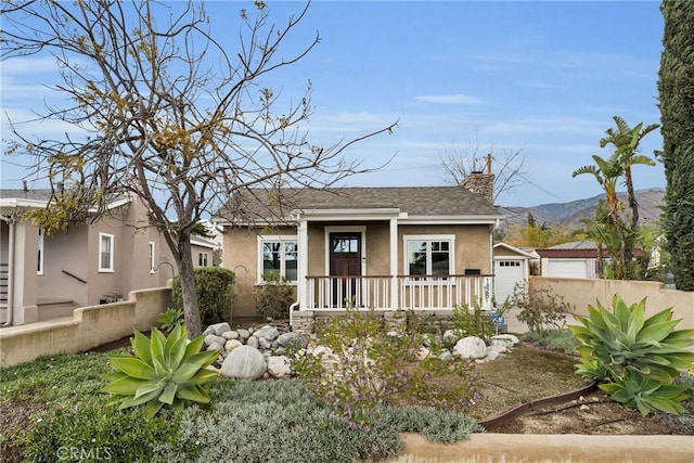 bungalow-style home with stucco siding, an outbuilding, a mountain view, a garage, and a chimney