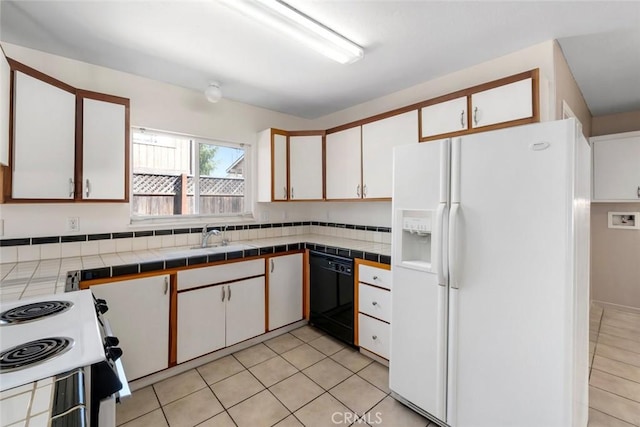 kitchen with white appliances, light tile patterned floors, a sink, tile counters, and white cabinetry