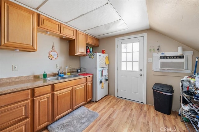 kitchen with lofted ceiling, freestanding refrigerator, a sink, light countertops, and light wood-type flooring