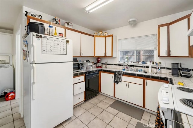 kitchen featuring light tile patterned floors, freestanding refrigerator, tile counters, dishwasher, and stainless steel microwave