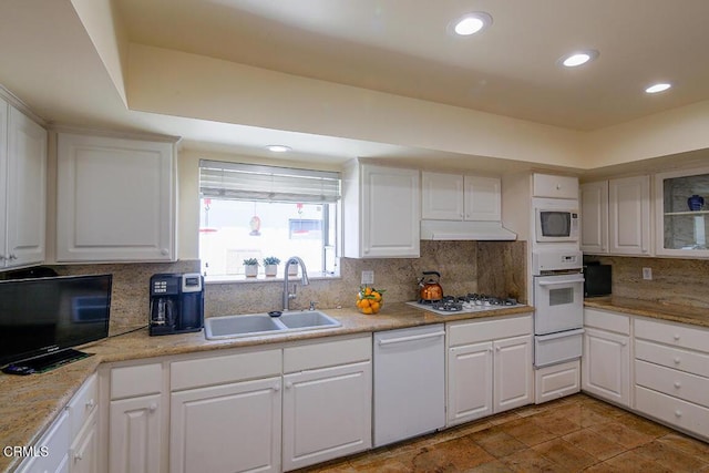 kitchen with a sink, under cabinet range hood, tasteful backsplash, white appliances, and white cabinets