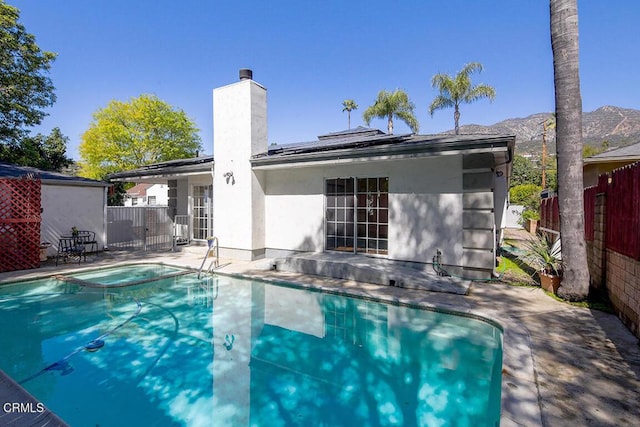 rear view of property featuring a patio, roof mounted solar panels, fence, an in ground hot tub, and a chimney