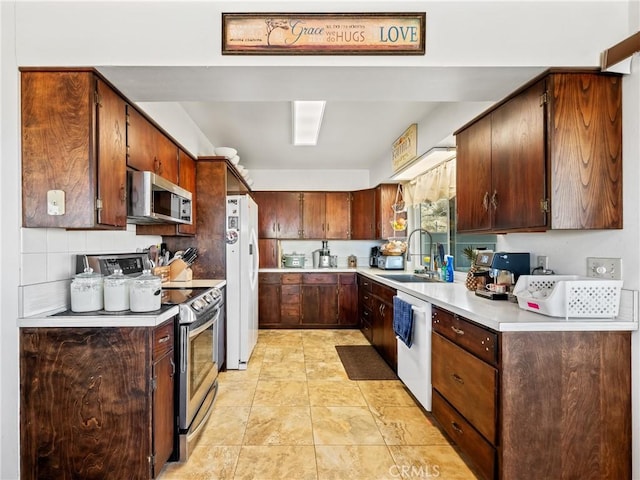 kitchen with a sink, tasteful backsplash, appliances with stainless steel finishes, light countertops, and light tile patterned floors