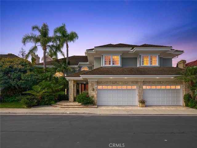 view of front of home featuring stone siding, an attached garage, driveway, and a tile roof