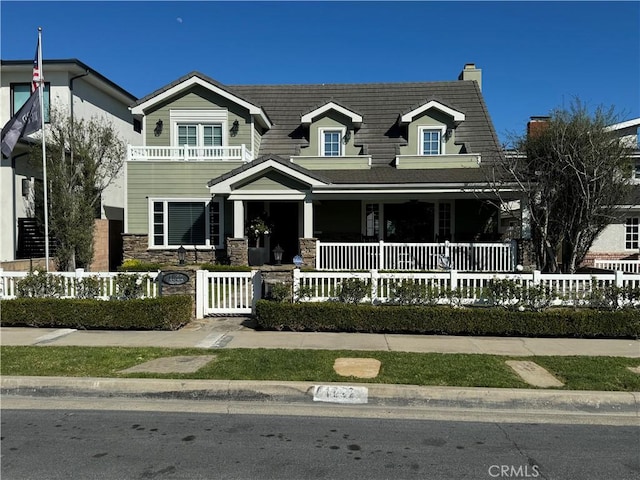 view of front of home with a porch, stone siding, and a fenced front yard