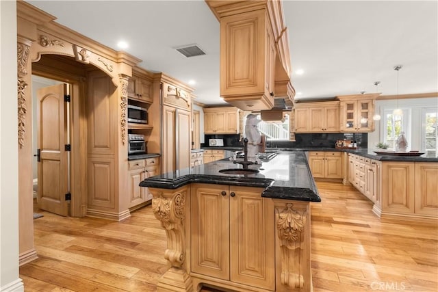 kitchen with visible vents, light wood finished floors, a center island with sink, and stainless steel microwave