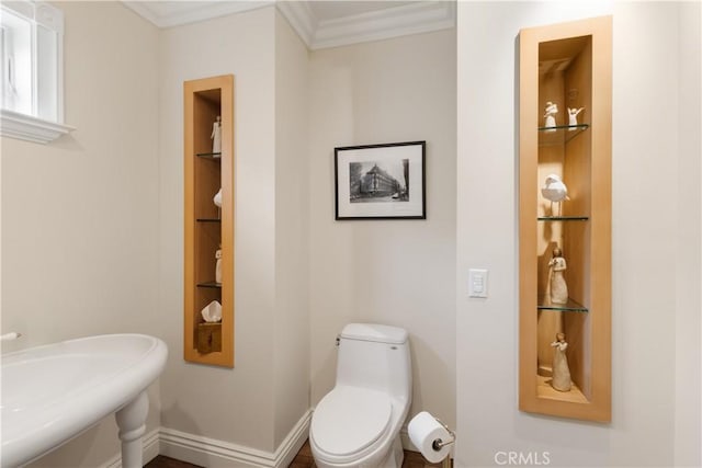 half bathroom featuring built in shelves, baseboards, toilet, ornamental molding, and a sink
