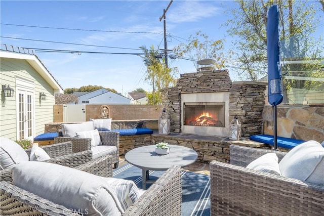 view of patio / terrace featuring an outdoor living space with a fireplace, fence, and french doors