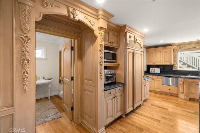 kitchen featuring a warming drawer, a sink, stainless steel microwave, dark countertops, and light wood-style floors