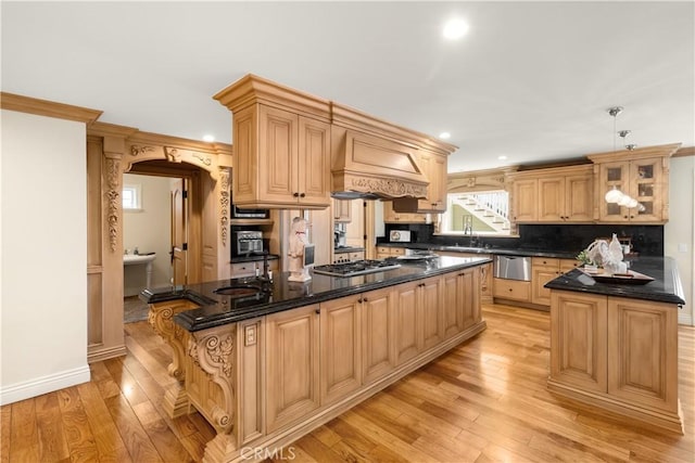 kitchen with premium range hood, light wood finished floors, a kitchen island, arched walkways, and a sink