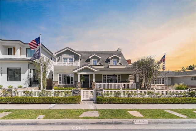 view of front of house with a balcony, a porch, stone siding, a fenced front yard, and a tile roof
