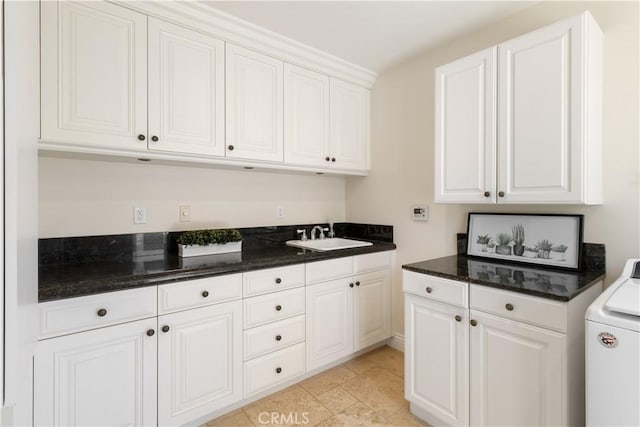 kitchen with white cabinetry, washer / clothes dryer, dark stone counters, and a sink