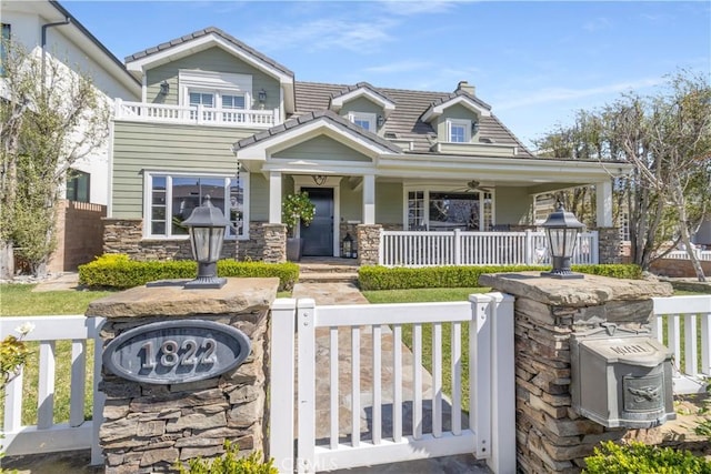view of front of house with a fenced front yard, stone siding, covered porch, and a tile roof