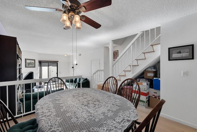 dining area with baseboards, stairway, light wood-style flooring, a textured ceiling, and a ceiling fan