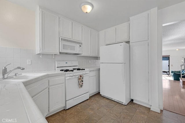 kitchen featuring a sink, white appliances, white cabinetry, and tile counters