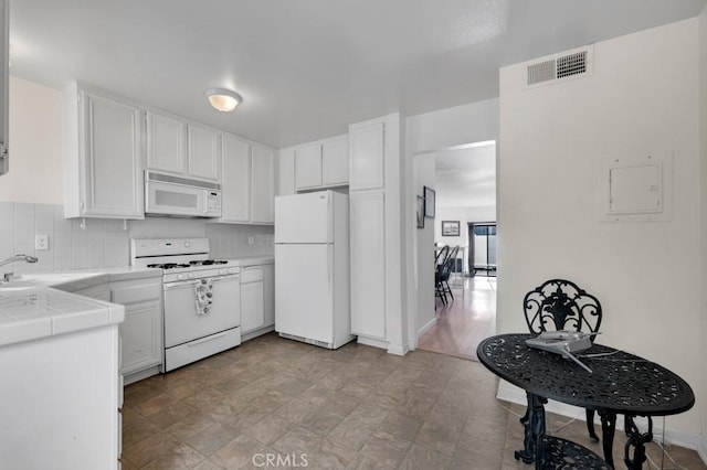 kitchen with white appliances, tile countertops, visible vents, white cabinetry, and backsplash